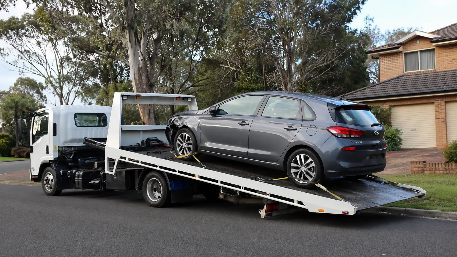 Tilt-tray tow truck winching a damaged Hyundai i30 onto its bed for free car removal in Sydney